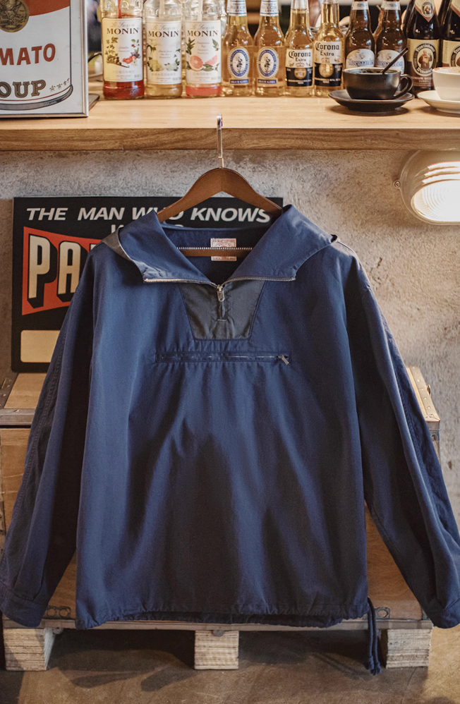 Navy cotton anorak with contrasting hood hanging on wood hanger in vintage interior.