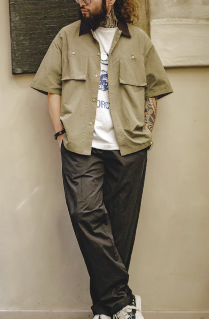 Full body view of man wearing khaki green retro waterproof utility shirt styled casually with black pants for outdoor and city wear