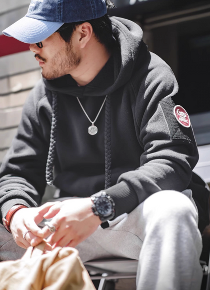 Man wearing RidgeLine Fleece Hoodie in black sitting casually showcasing sleeve patch detail, ribbed cuffs, and relaxed fit design
