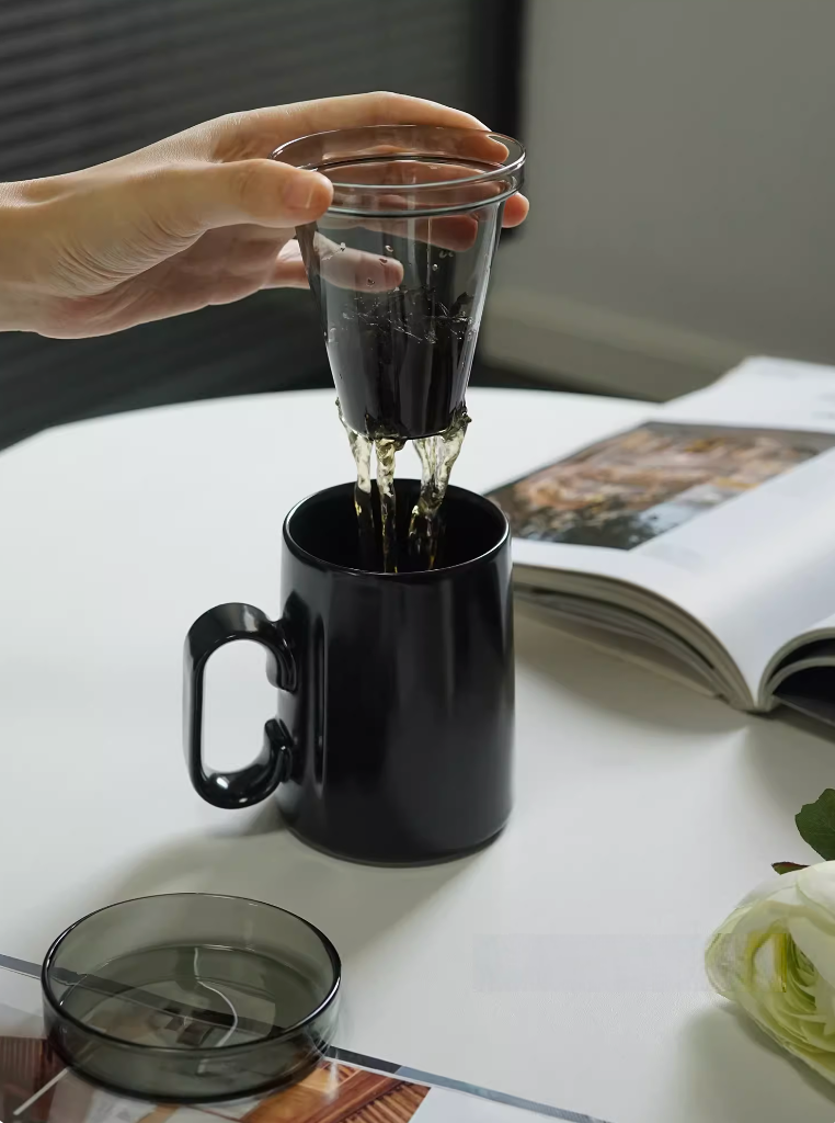 Black ring-handle ceramic tea mug in use with glass infuser, tea being poured and filtered into mug, lifestyle brewing scene