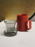 Red ring-handle ceramic tea mug with glass infuser and lid placed separately, front view showing mug, filter, and lid components