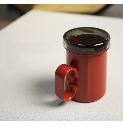 Red ring-handle ceramic tea mug with lid attached, angled side view highlighting ergonomic ring handle and smooth glazed finish
