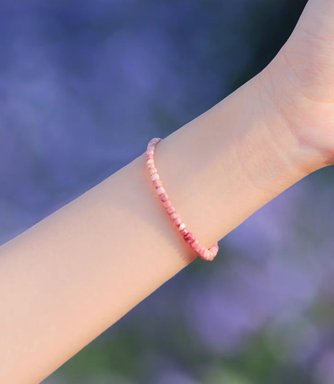 Rose rhodonite bracelet worn on wrist in natural outdoor lighting showing delicate pink bead gradient and slim design