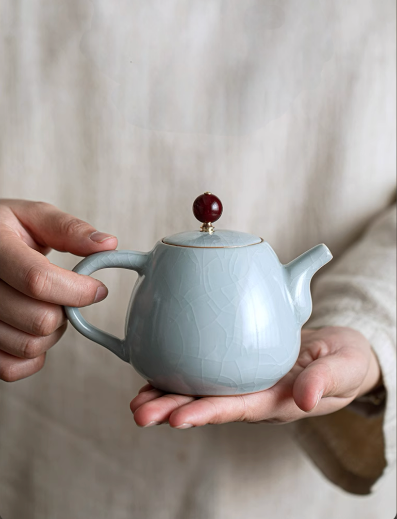 Ru Kiln Celadon Mini Teapot in light blue front view held in hands displaying smooth rounded body and crackle glaze texture