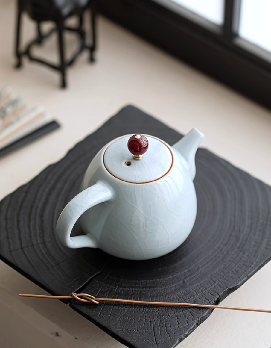 Ru Kiln Celadon Mini Teapot in light blue color top view showing crackle glaze surface and red bead lid knob placed on a black textured tray