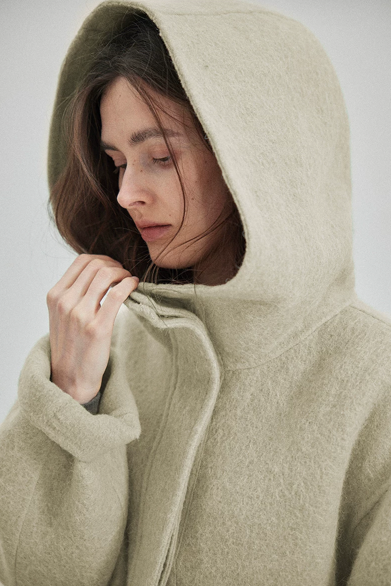 Close-up of a Sage double-face wool coat worn with the hood up, showing the brushed surface