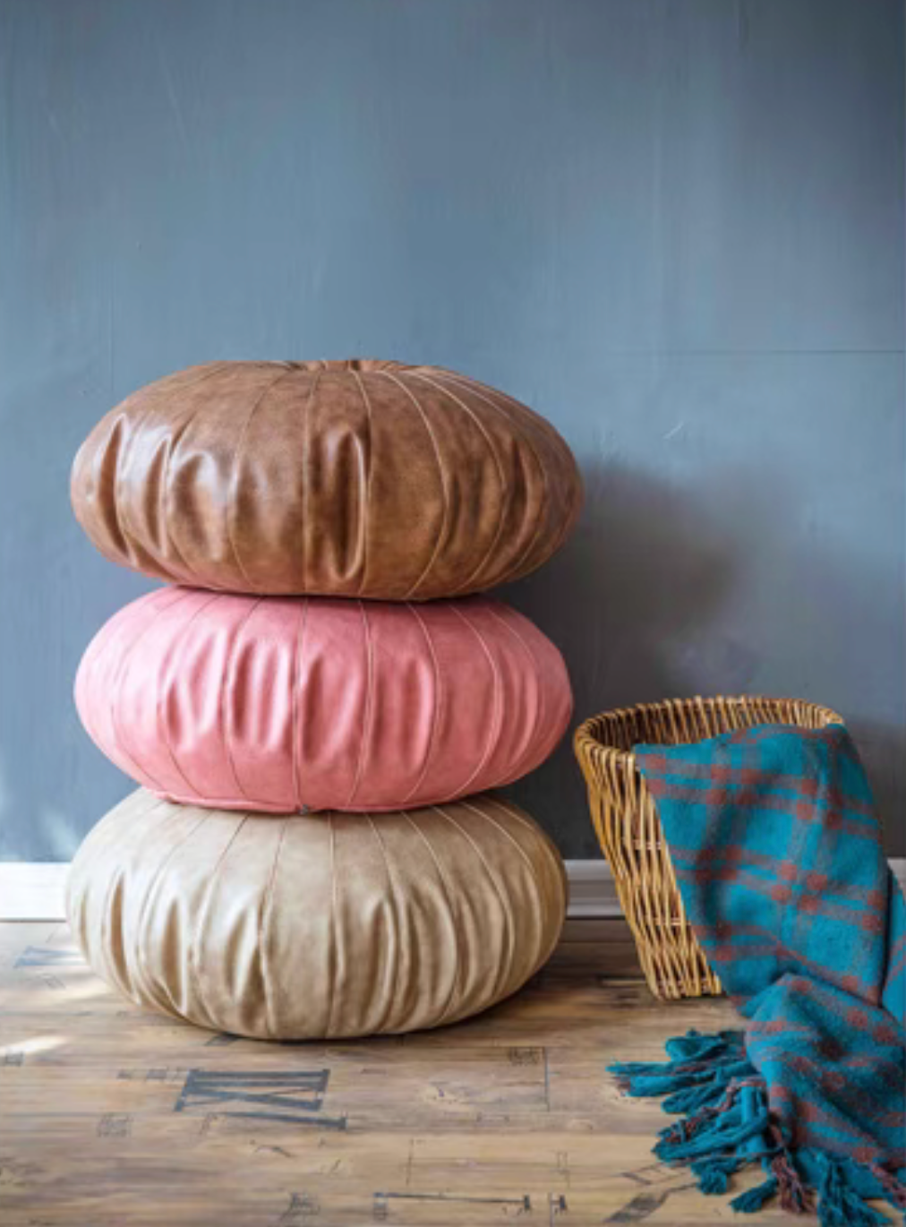 Scandinavian round floor cushions in camel, pink, and ivory stacked together on wooden floor beside a basket