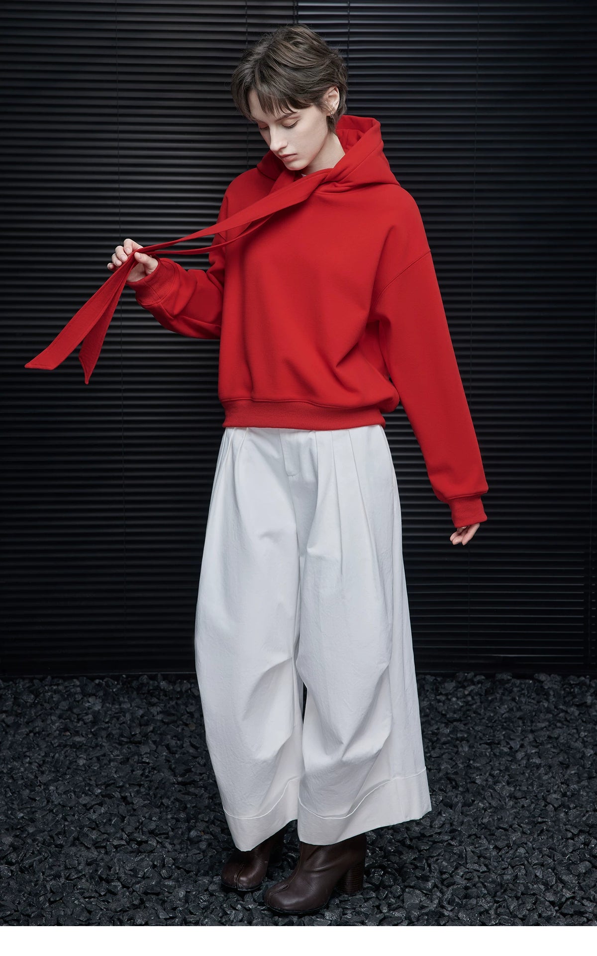 Full-length look of Scarlet Red tie-neck hoodie with one ribbon swinging, paired with white pleated trousers