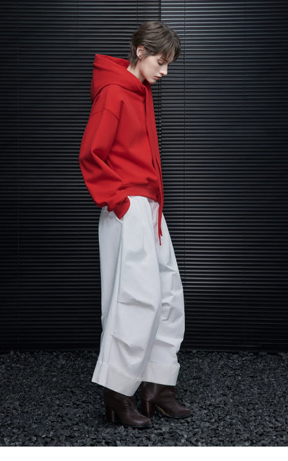 Side profile of woman in Scarlet Red tie-neck hoodie with white wide-leg cuffed trousers and brown boots