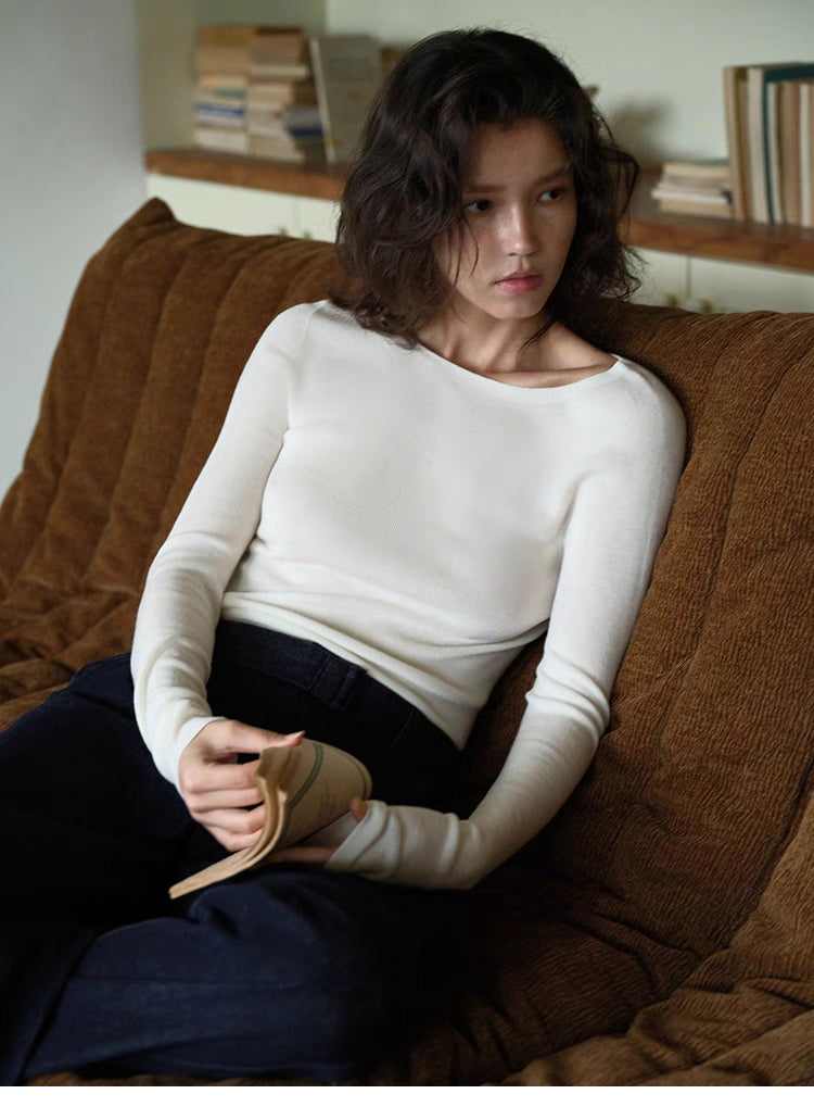 Model seated on sofa wearing vanilla white seamless merino sweater, showing close-to-body fit and soft drape