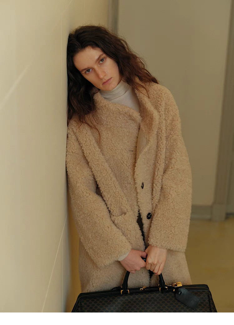 Angled front view of Sierra Luxe Shearling Coat in beige apricot styled with handbag, showcasing soft shearling texture, button front, and relaxed fit