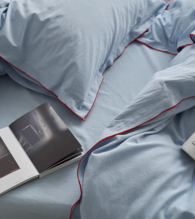 Light blue cotton pillow shams with red edge stitching from Skyline bedding set shown in close lifestyle bedding detail