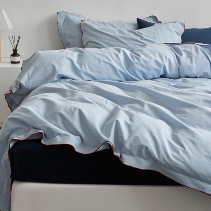 Skyline bedding set in light blue with red edge stitching paired with navy blue flat sheet creating layered modern bedding style