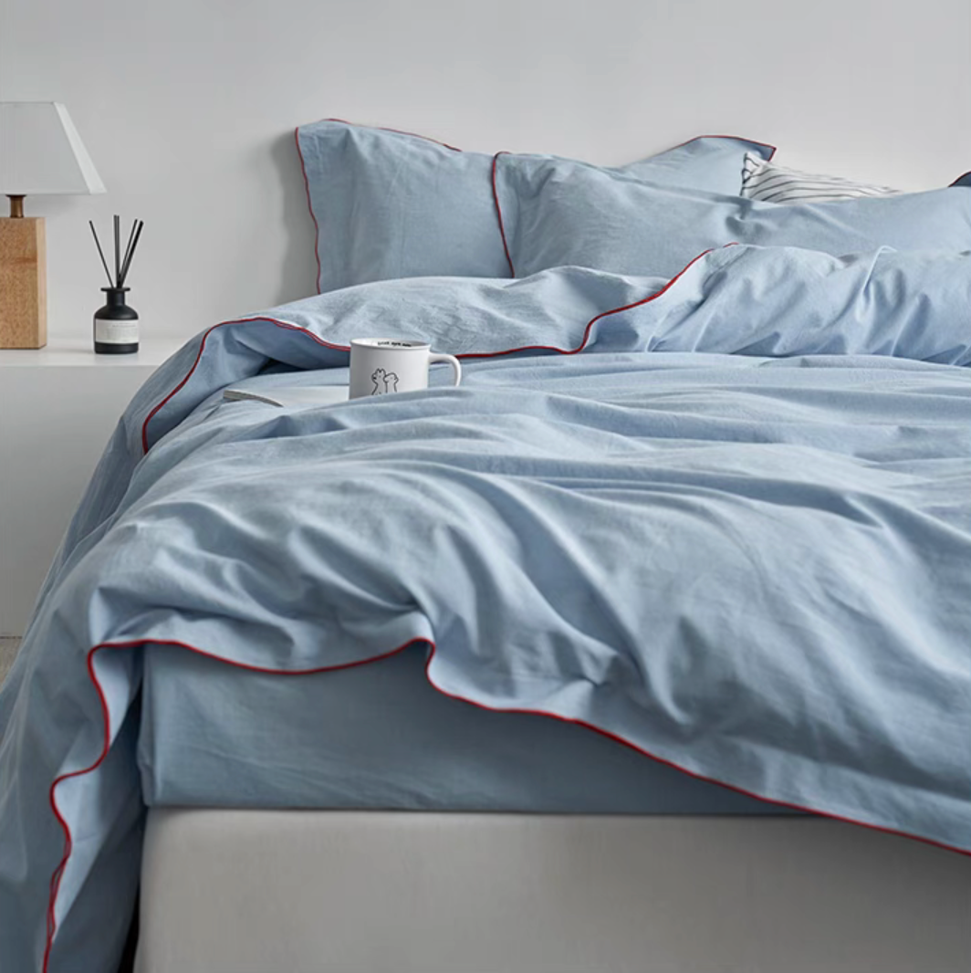Skyline edge-stitched cotton duvet, sheet and sham set in light blue with red edge stitching styled on bed creating a soft breathable bedroom look
