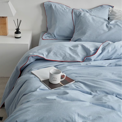 Skyline light blue cotton duvet, sheet and sham set with red edge stitching styled on bed with cup and book creating relaxed bedroom scene