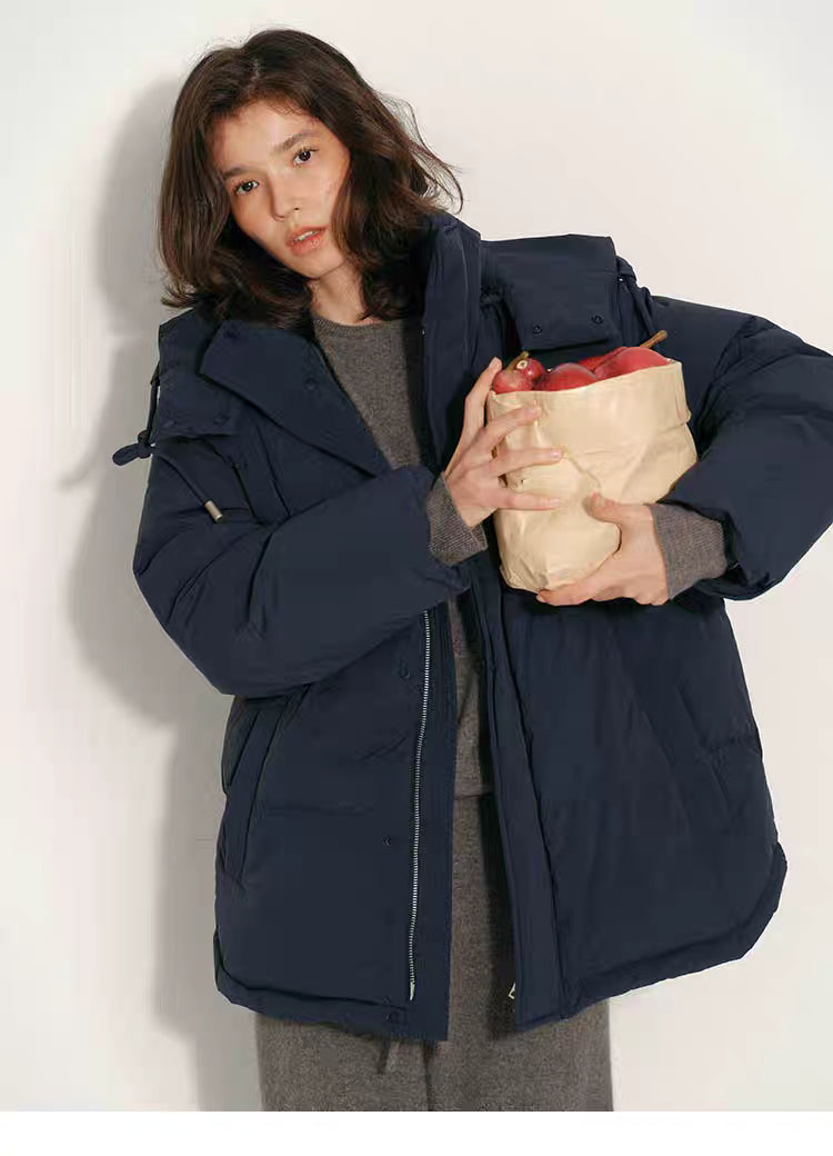 Model wearing navy blue puffer jacket holding apples in both hands, front-facing pose.