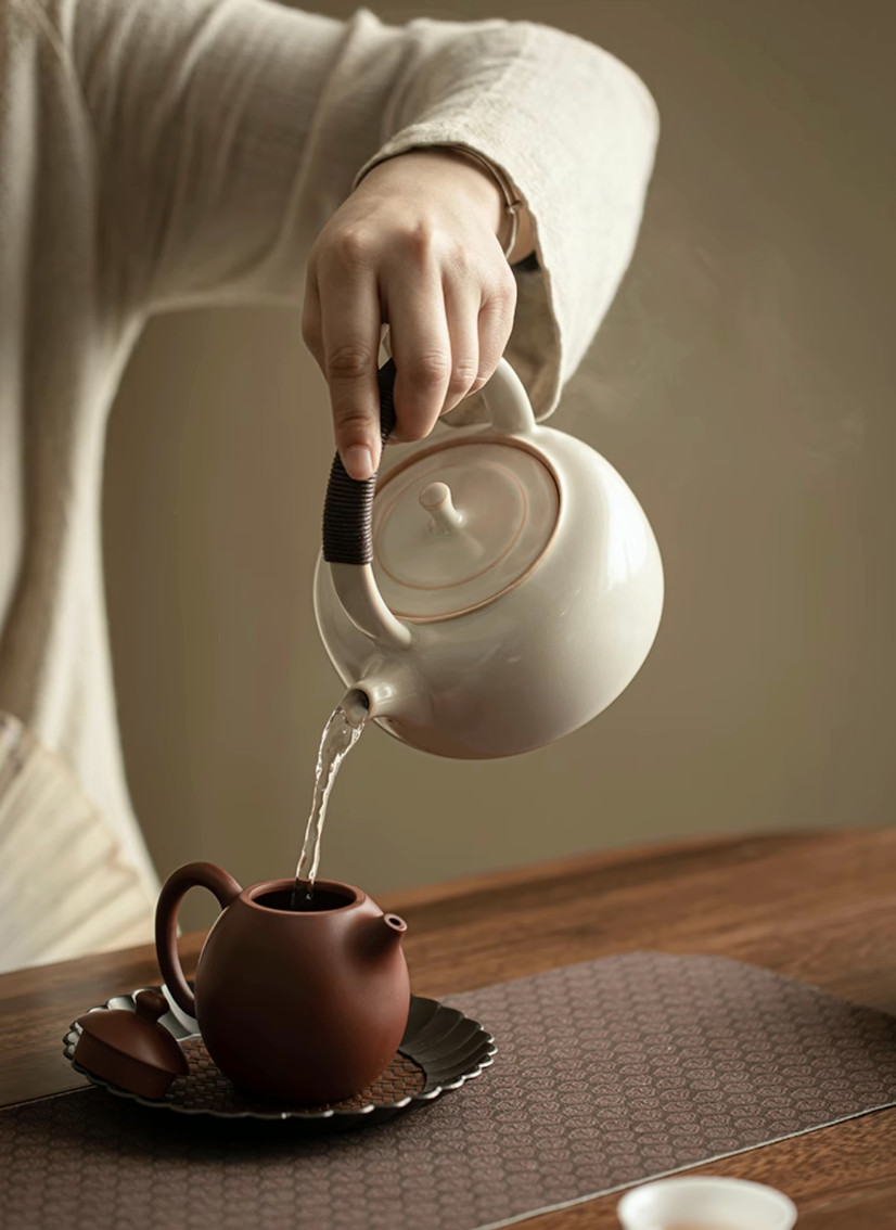 Soda Glaze Ceramic Teapot in off-white pouring hot water into a small clay teapot showing controlled spout flow