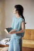 Model wearing Lake Blue merino sleeveless vest in side view holding a book, showcasing textured knit, soft drape, and relaxed fit silhouette
