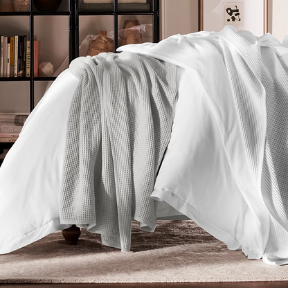 Light gray waffle gauze cotton blanket draped across the side of a bed creating a cozy layered bedding look.
