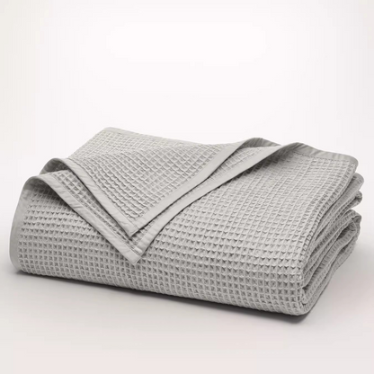 Folded light gray waffle gauze cotton blanket displaying breathable waffle weave and soft cotton construction.