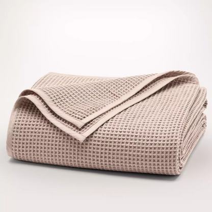 Folded light pink waffle gauze cotton blanket showing breathable textured fabric and clean stitched edges.