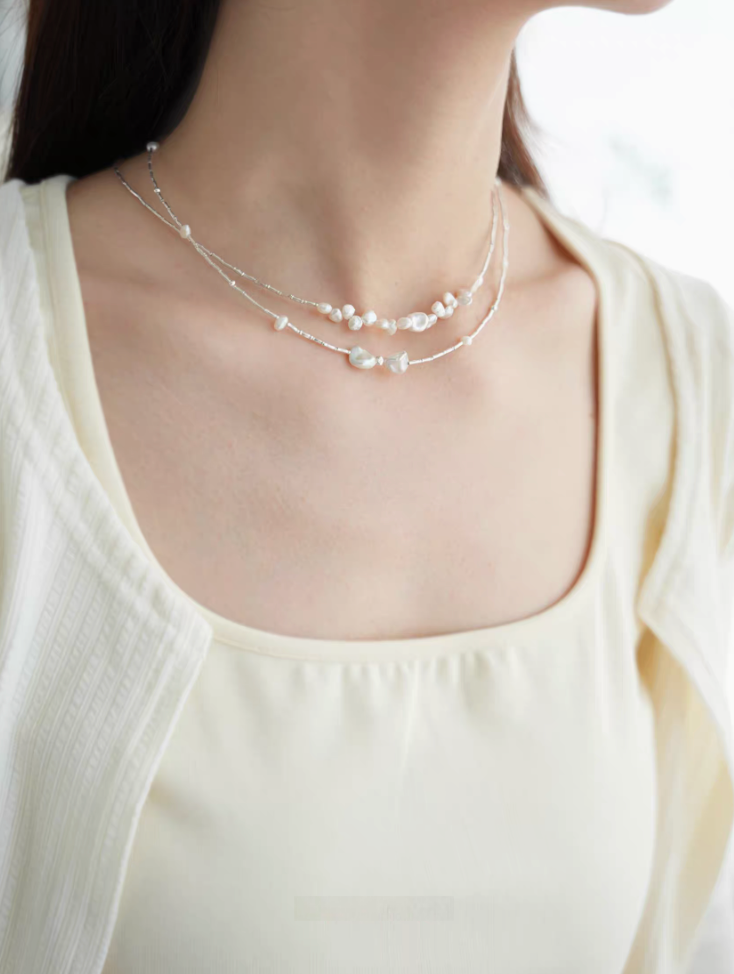 Soft white baroque pearl silver choker worn layered with delicate chain necklaces on neckline