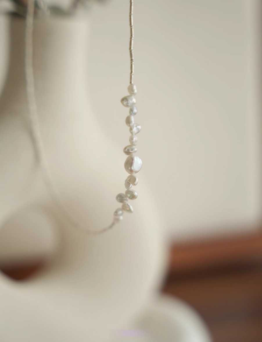 Soft white baroque pearl silver choker hanging with vertical pearl cluster detail in soft natural lighting