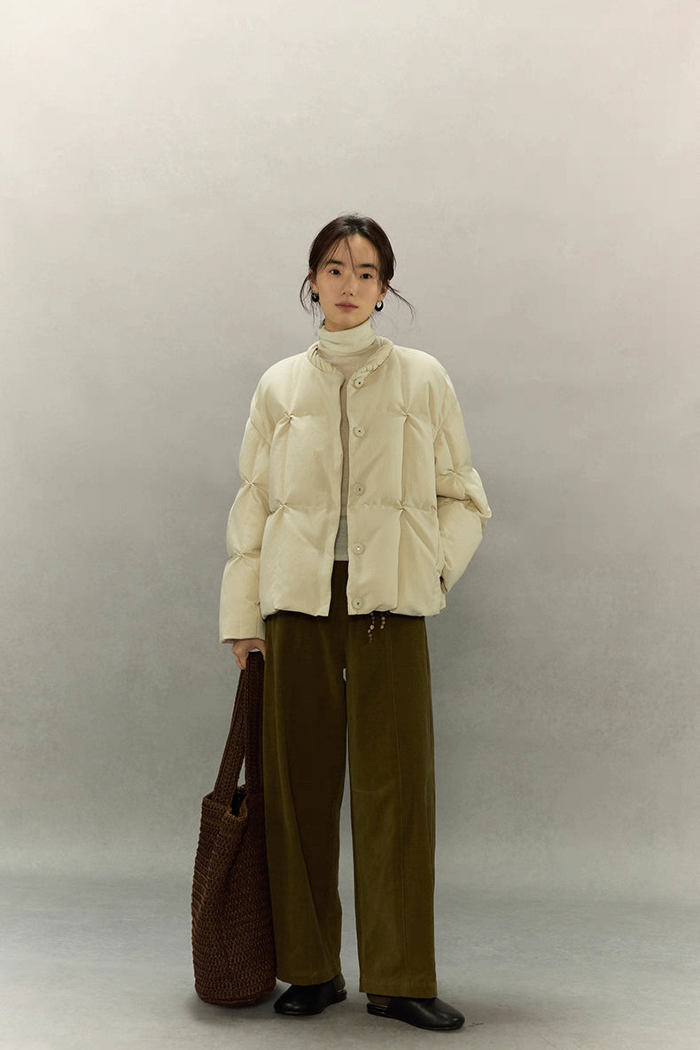 Full-body front view of model wearing cream beige SoftCloud down jacket with wide-leg olive pants and brown tote bag.