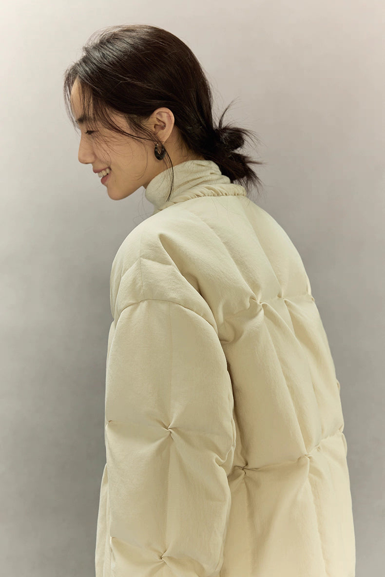 Close-up of shoulder and upper back of cream beige SoftCloud down jacket showing soft matte fabric and tufted quilting texture.