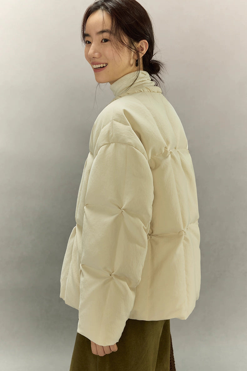 Side-back view of cream beige SoftCloud down jacket highlighting dough-puff quilting and short boxy silhouette.