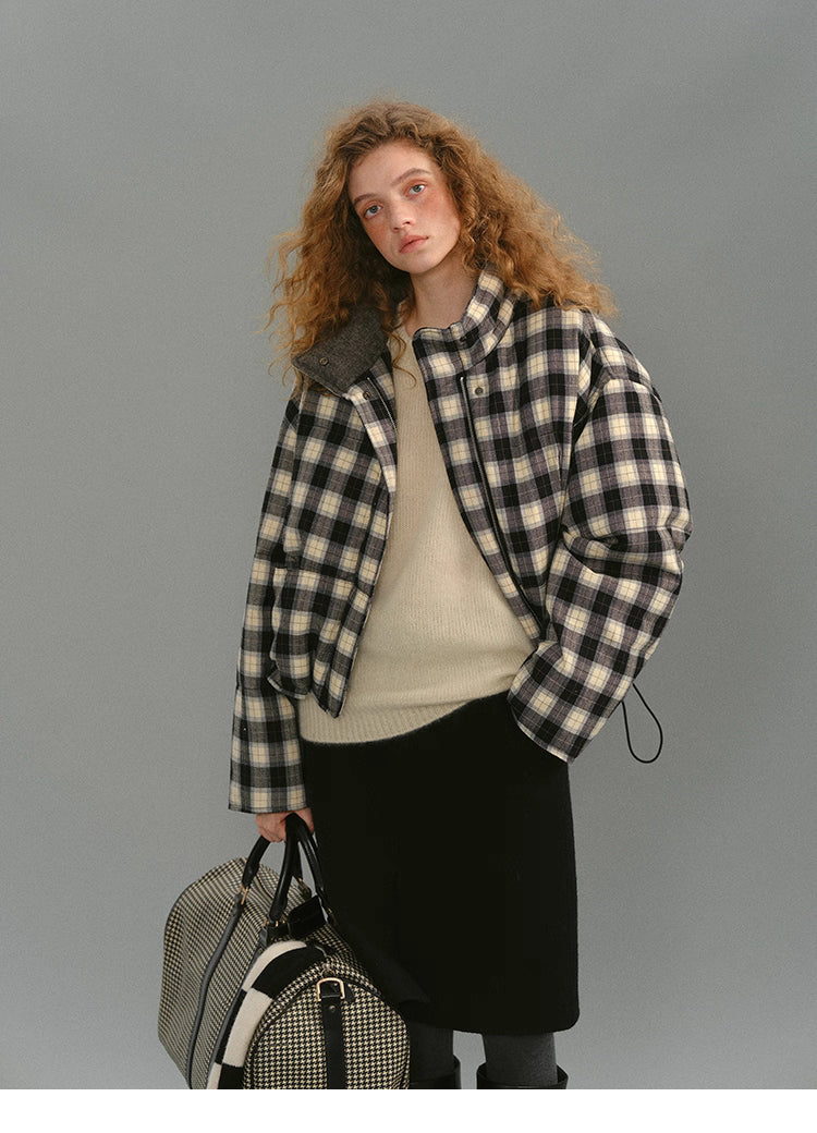 Model wearing the SoftGrid wool check puffer jacket, front view with collar open, paired with a cream sweater and black skirt, holding a check weekender bag.