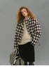 Model wearing the SoftGrid wool check puffer jacket, front view with collar open, paired with a cream sweater and black skirt, holding a check weekender bag.