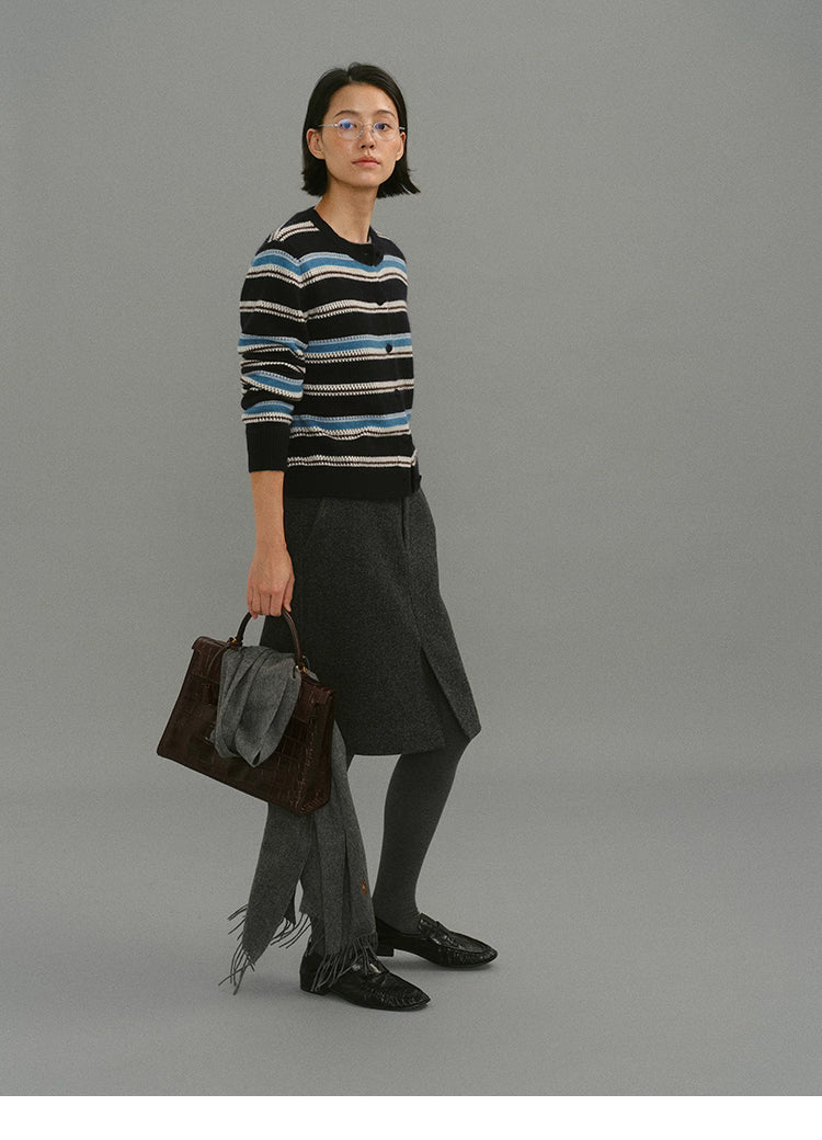 Side-walking shot of the black-blue striped cardigan styled with a charcoal skirt and structured handbag.