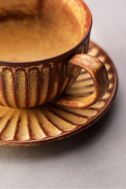 Close-up of yellow striped ceramic cappuccino cup handle and saucer showing textured glaze and handcrafted detail