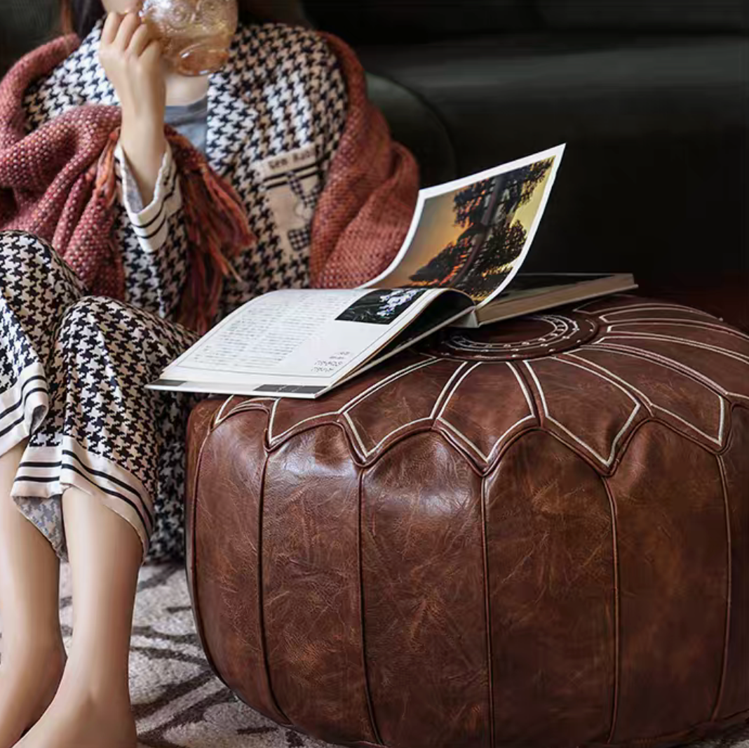 Camel faux leather pouf ottoman used as a footrest with a book in a cozy living room setting