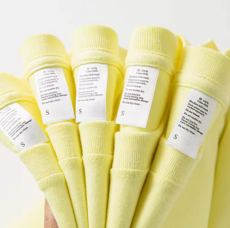 Close-up of lemon yellow cotton tee care labels showing fabric and size details