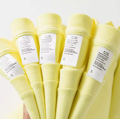 Close-up of lemon yellow cotton tee care labels showing fabric and size details