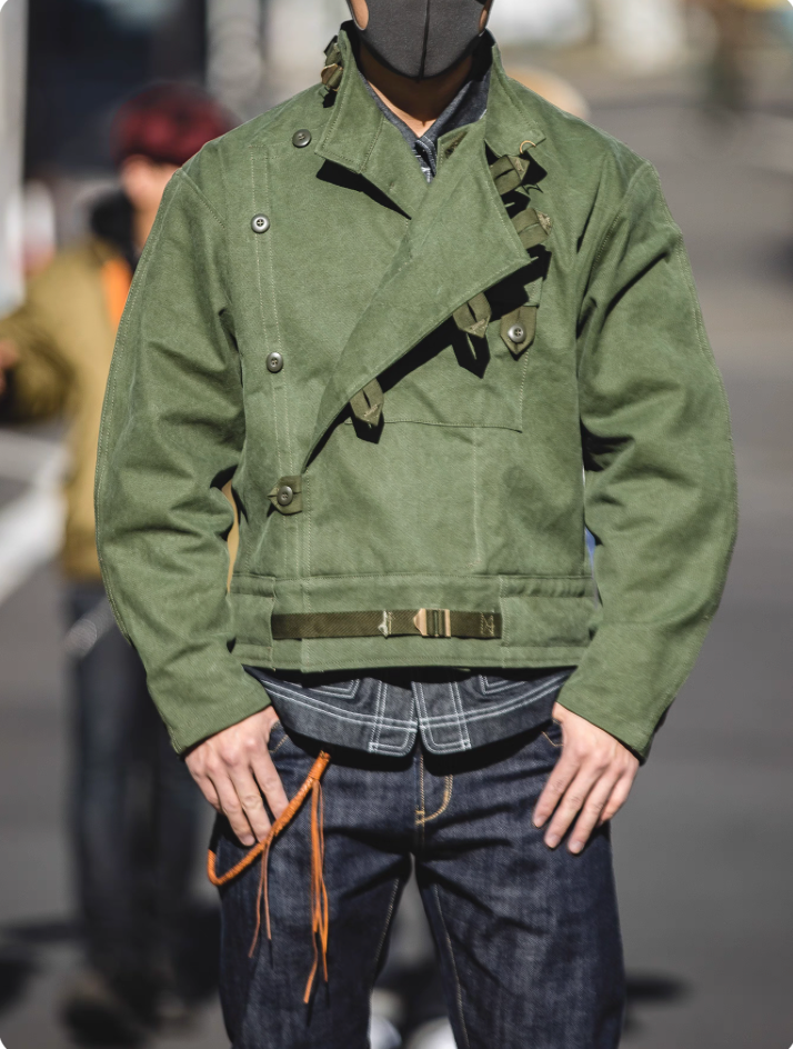 Model wearing Swedish military motorcycle jacket outdoors – vintage green canvas with asymmetrical closure.
