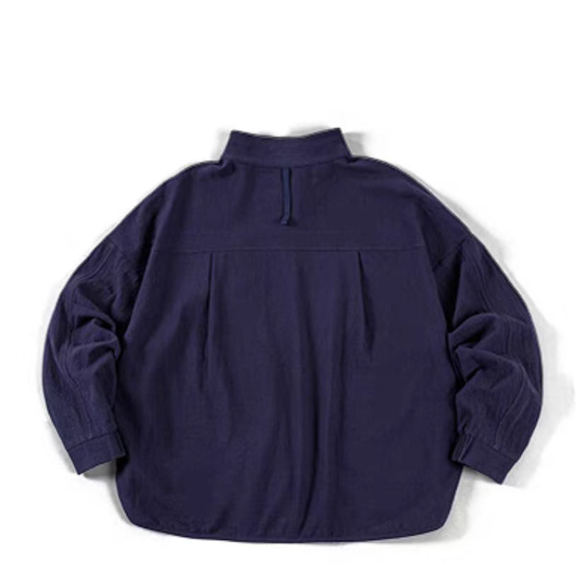Blue textured cotton polo shirt flat lay back view showing curved hem, back pleat detail, and relaxed silhouette