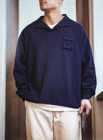 Blue textured cotton polo shirt worn by model front view showing relaxed fit, curved hem, and casual styling with light pants