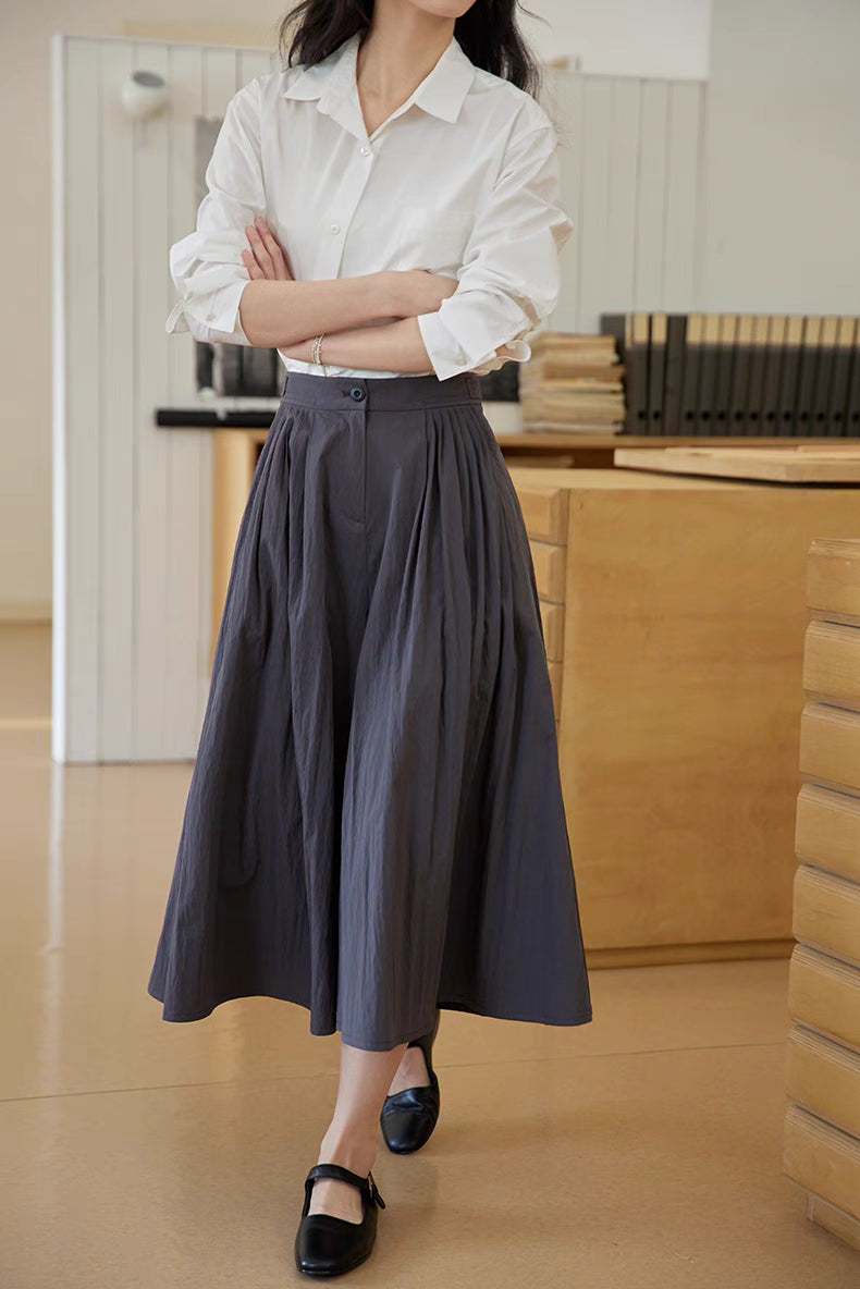 The Poised Pleated Midi Skirt in charcoal gray shown in mid-length walking view, highlighting fluid movement, structured pleats, and A-line shape