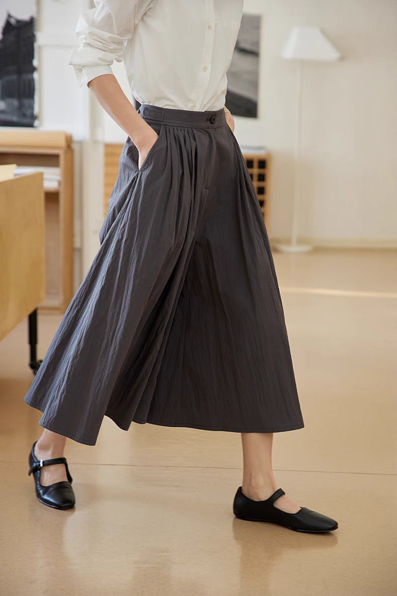The Poised Pleated Midi Skirt in charcoal gray shown in motion with side pocket detail, A-line silhouette, and natural drape of pleated fabric