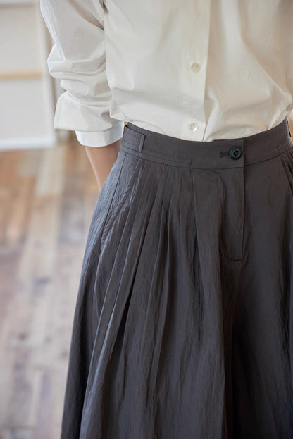 Close-up of The Poised Pleated Midi Skirt in charcoal gray featuring waistband button closure, fine pleats, and crinkled fabric texture detail
