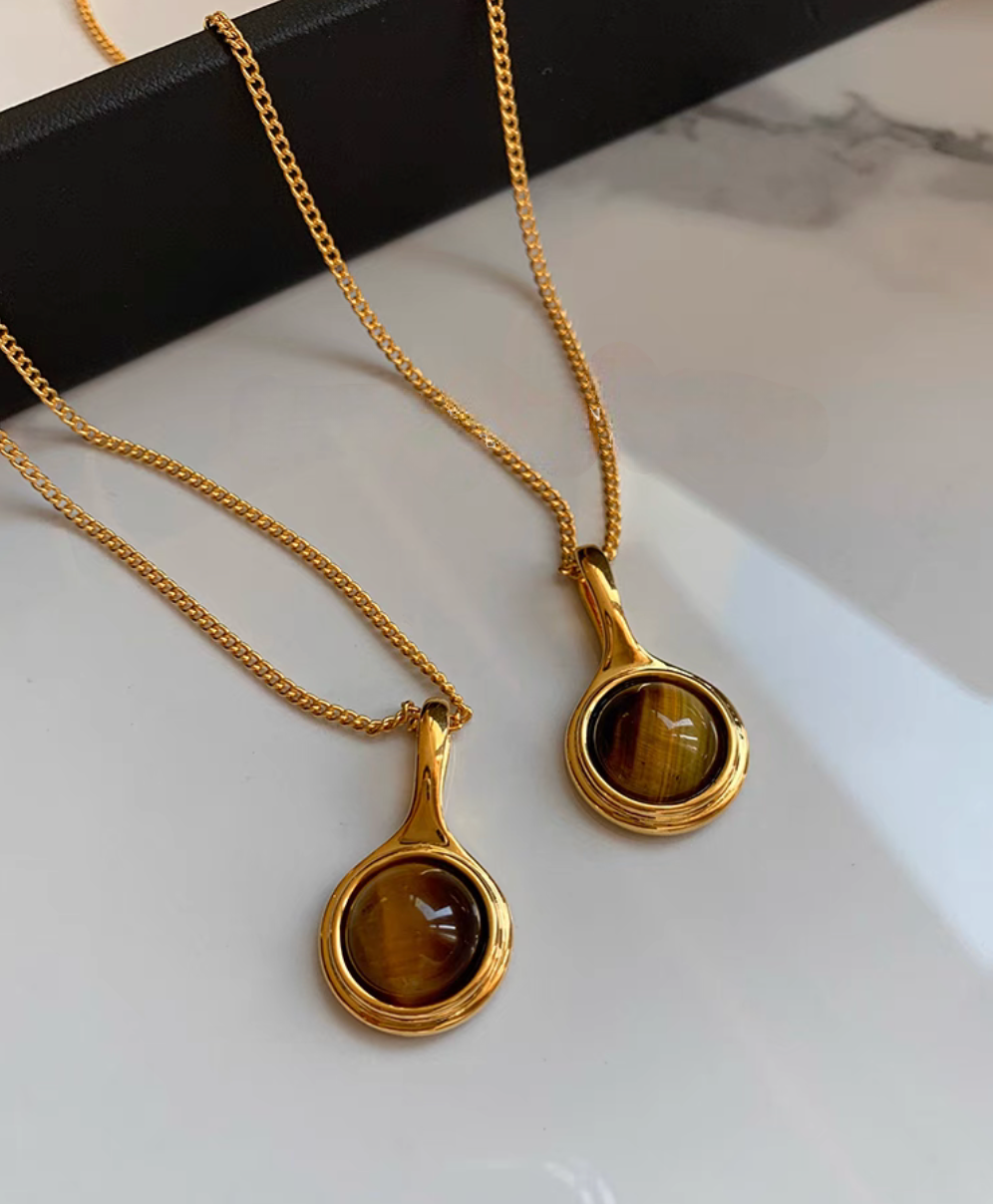Close-up of tiger eye gemstone pendant set in 24K gold-plated brass with polished round stone on gold chain
