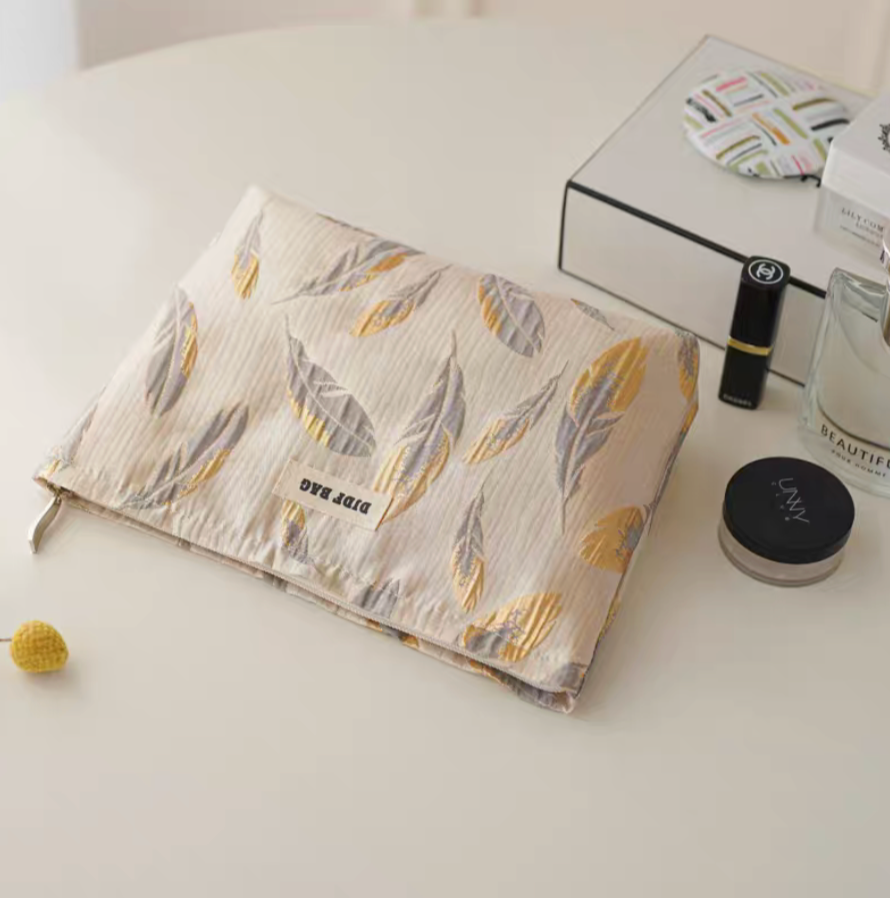 Timeless Elegance Portable Makeup Bag in golden feather pattern laid flat with makeup products beside on clean surface