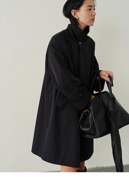 Side view of Black Timeless Trench Coat with model holding bag showing relaxed fit, long sleeves and practical styling