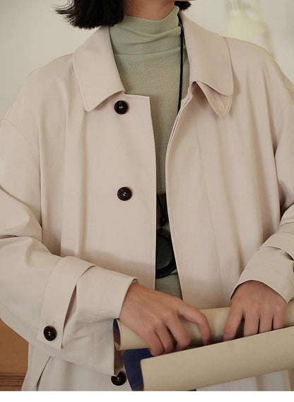Tea Beige Timeless Trench Coat front view with model at desk showing clean tailoring, button closure and soft structure