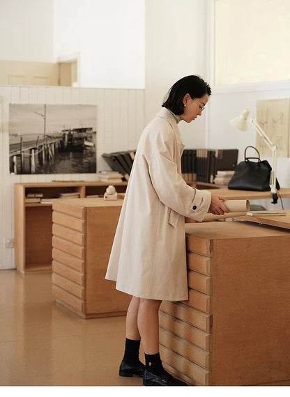 Side back view of Tea Beige Timeless Trench Coat in office setting showing mid-length cut and relaxed straight silhouette