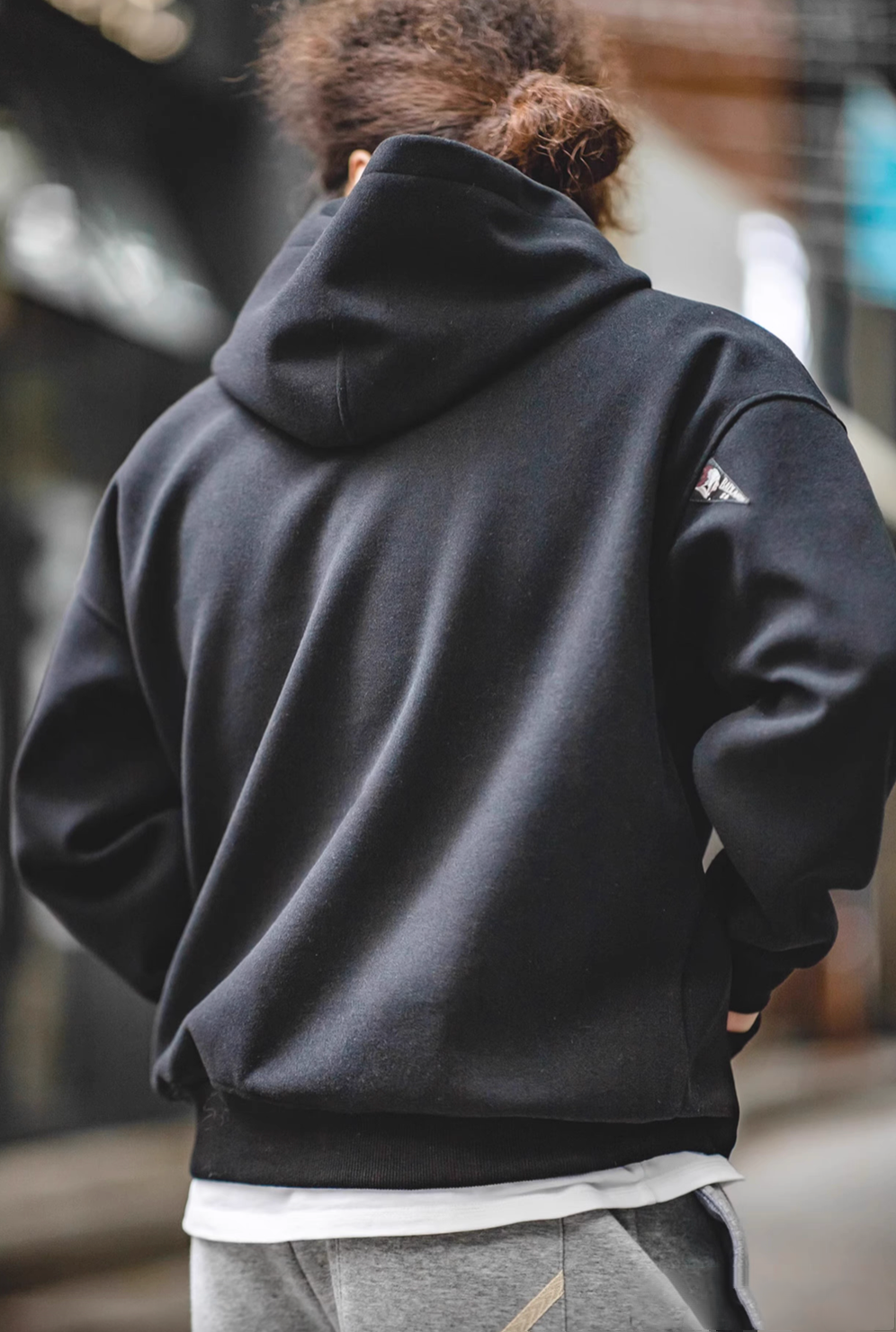 Back view of model wearing Trailblazer Pullover Hoodie in black showing hood structure and relaxed street style fit