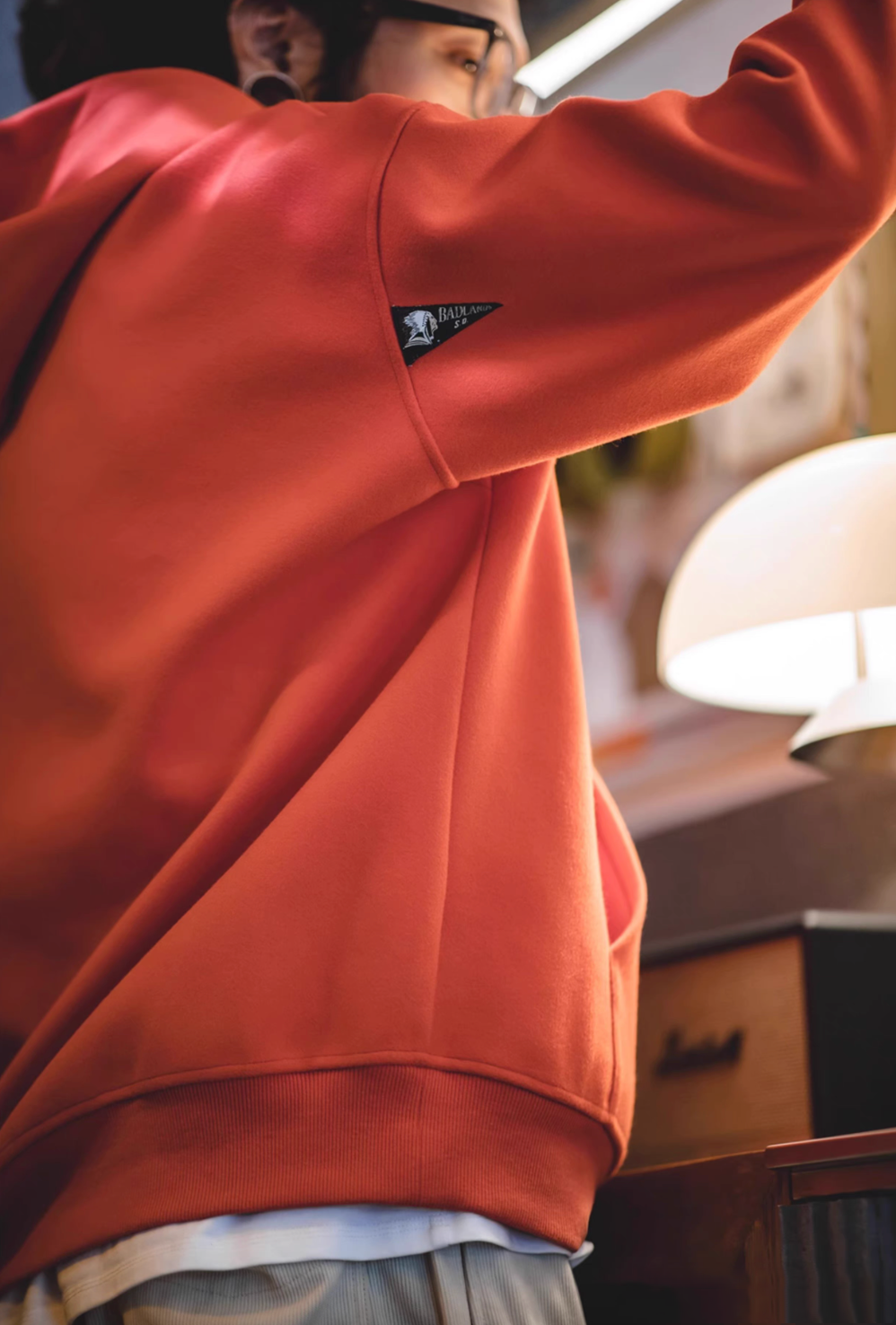 Close-up of Trailblazer Pullover Hoodie in orange showing sleeve logo detail and soft fabric texture